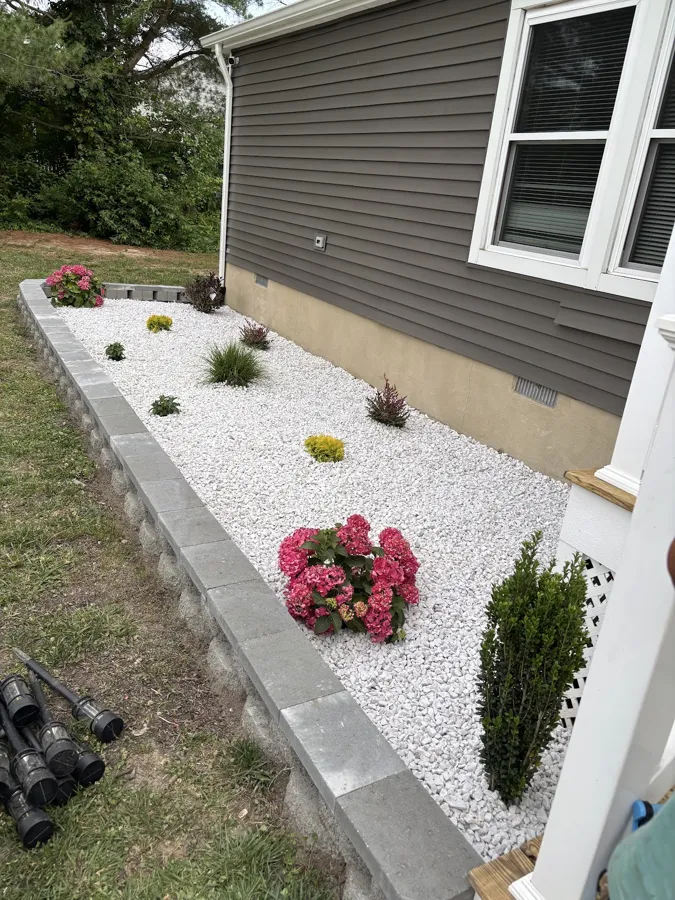 White decorative stone bed with a gray block border along the side of a house, planted with hydrangeas