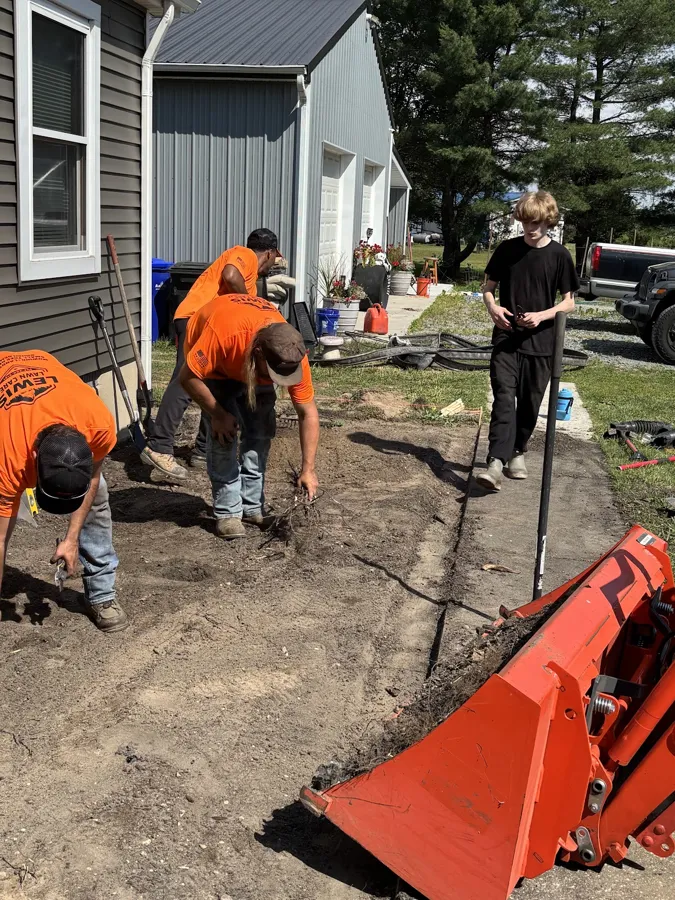 Crew planting beside a house, with the compact tractor's orange loader bucket in front