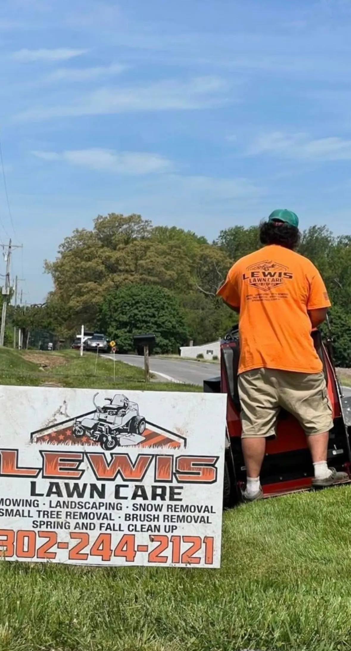Lewis Lawn Care mowing a roadside lawn next to the company yard sign